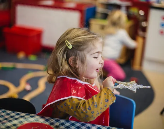 A girl in a red apron playing with a sparkly wand