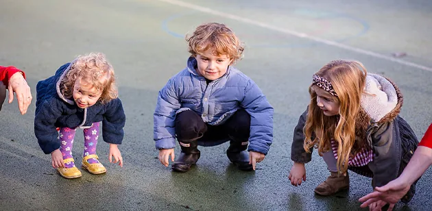 Three children crouching to look at something in the playground